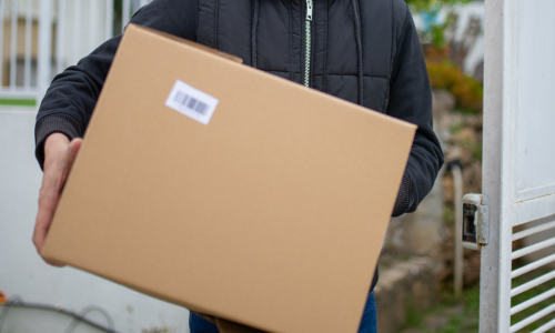 A man walking into his house with a box.